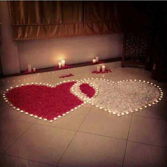 کف اتاق خواب عروسی که روی آن به وسیله دو قلب سفید و قرمز که از گلبرگ و شمع های کوچک درست شده اند، دیزاین شده اشت